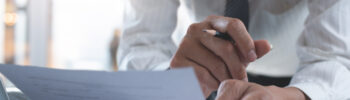 Businessman reading a printed out payslip, holding a pen. He is wearing a shirt and tie.